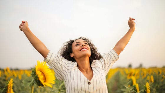 Photo of a woman in a sunflower field with hands raised